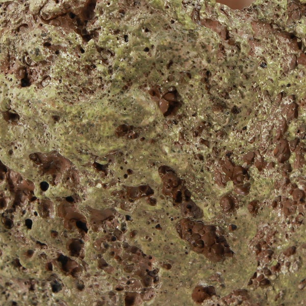 Nahaufnahme eines porösen Lavasteins mit unregelmäßiger Oberfläche, rötlich-braunem Gestein und grünlichem Mineralbelag.