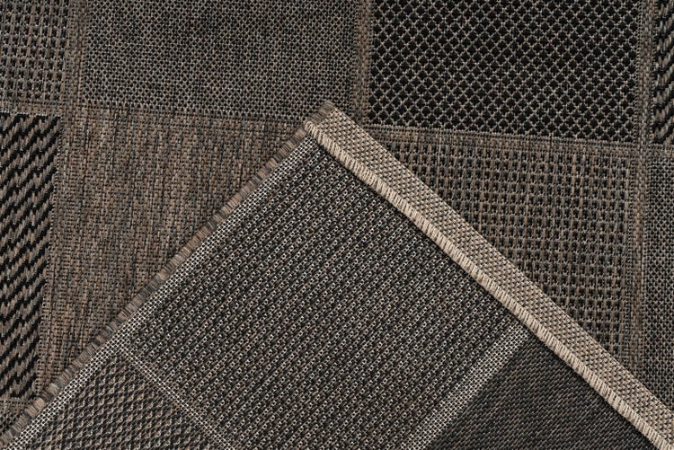 Nahaufnahme eines Flachgewebe-Teppichs mit Patchwork-Design aus verschiedenen geometrischen Mustern und umgeschlagener Ecke mit Kettelrand.