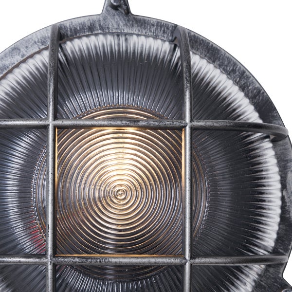 Eingeschaltete Außenleuchte mit Metallgitter und geriffeltem Glas im industriellen Stil.