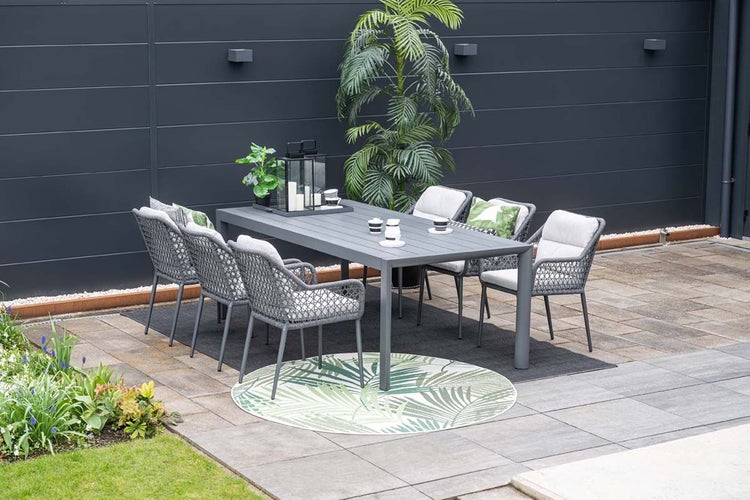 Modernes Gartenmöbel-Set bestehend aus grauem Aluminiumtisch und sechs Sesseln mit Kordelgeflecht auf einer gepflasterten Terrasse.
