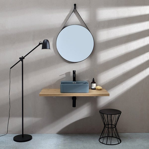 Modernes Badezimmer mit rundem Spiegel, rechteckigem Aufsatzwaschbecken auf einer Holzkonsole, Stehlampe und einem Drahthocker.