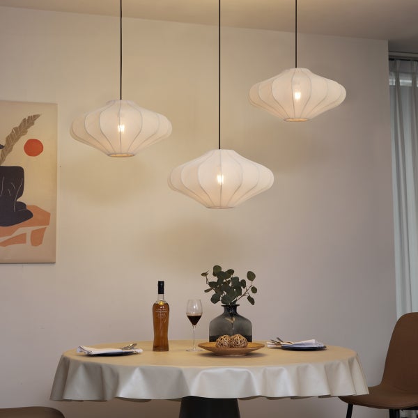 Drei weiße Pendelleuchten in Kokonform über einem gedeckten runden Esstisch in einem hellen, modern eingerichteten Raum.