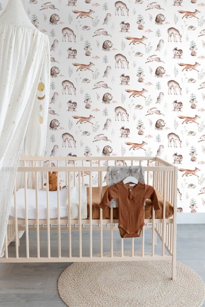 Kinderzimmer mit Babybett vor einer Tapete mit Waldtiermotiven.