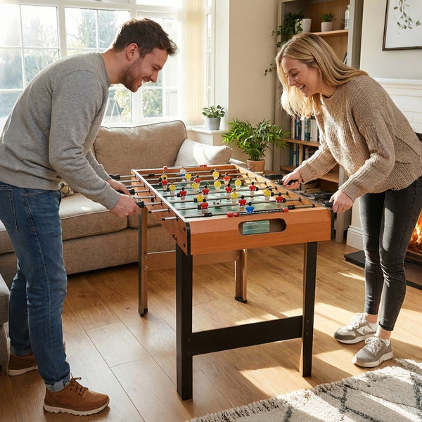 Ein Paar spielt an einem hölzernen Kickertisch in einem hellen Wohnzimmer mit Holzboden.