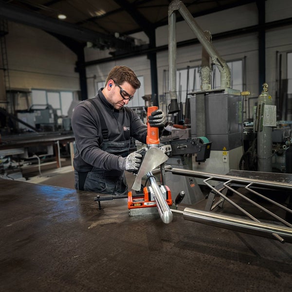 Mann verwendet Rohrbandschleifer-Vorsatz für Winkelschleifer zum Schleifen eines Edelstahl-Handlaufs mit Schutzbrille und Handschuhen.