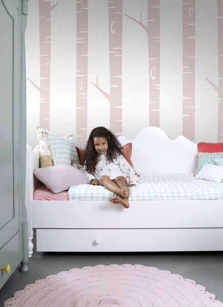 Helles Kinderzimmer mit weißem Bett, gemusterten Kissen und Birkenmuster-Tapete.