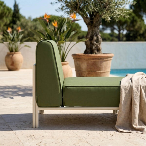 Modernes Gartensofa mit grünen Polstern und weißem Metallrahmen auf einer Steinterrasse am Pool mit Olivenbaum und Strelitzien in Kübeln.