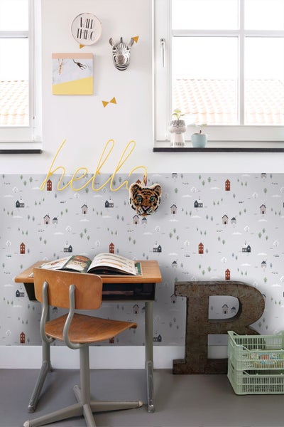 Hell gestaltetes Kinderzimmer mit Mustertapete, Holzschreibtisch, Stuhl und verschiedenen Dekorationselementen an der Wand.