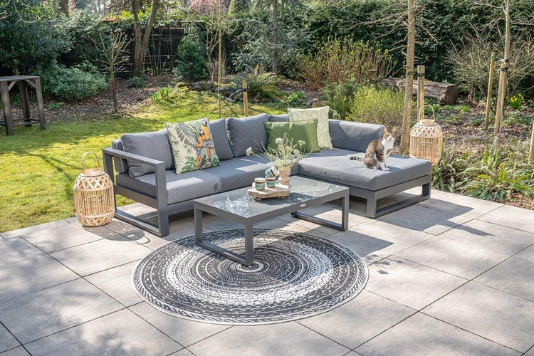 Moderne Garten-Lounge-Gruppe mit grauem Ecksofa, grauen Polstern und passendem Couchtisch mit Glasplatte auf einer Terrasse.