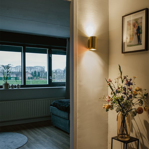 Flur mit Wandleuchte, Blumenstrauß, gerahmtem Bild und Blick in ein Zimmer mit Fenster.