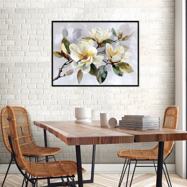 Gerahmtes Bild mit Magnolienblüten an einer Ziegelwand über einem Holztisch mit Rattanstühlen.