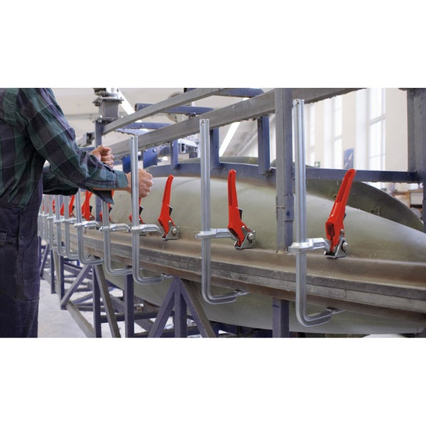 Eine Person befestigt mit Schraubzwingen ein Werkstück an einer Werkbank.