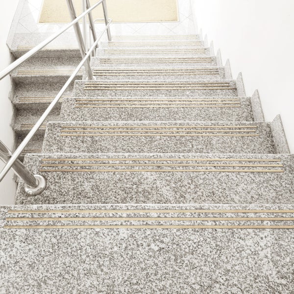 Steintreppe mit rutschfesten Profilschienen aus Metall und Edelstahlgeländer in einem hellen Treppenhaus.