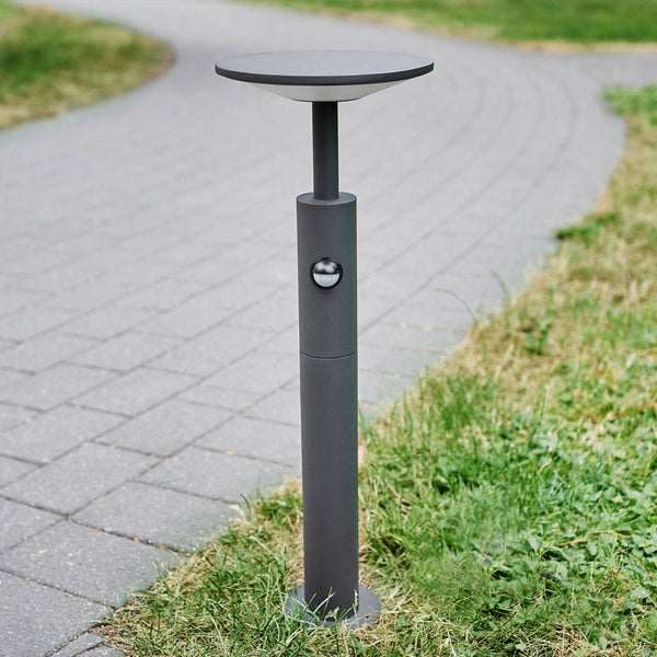 Moderne LED-Wegleuchte aus anthrazitfarbenem Aluminium mit Bewegungsmelder an einem gepflasterten Gartenweg.