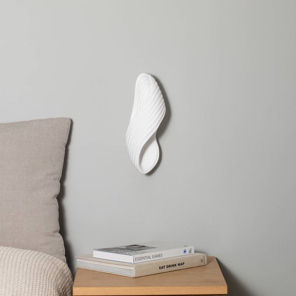 Weiße Wandleuchte mit organischer Form über einem Nachttisch aus Holz mit Büchern in einem minimalistischen Schlafzimmer.