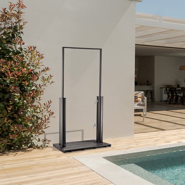 Eine freistehende Gartendusche aus Metall mit Bodenplatte und integrierter Fußdusche auf einer Terrasse neben einem Swimmingpool.