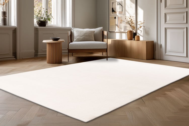 Ein schlichter, einfarbiger Teppich in einem modern eingerichteten Wohnzimmer mit Fischgrätparkett, Sessel und Beistelltisch.