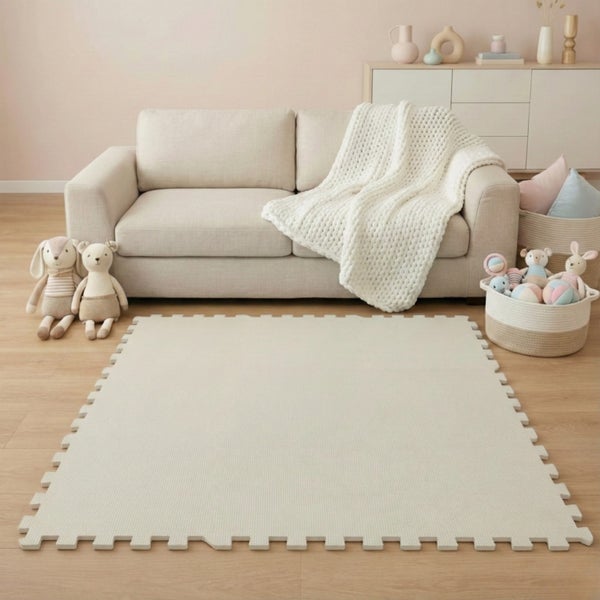 Beige Schaumstoff-Spielmatte im Puzzle-Design in einem hellen Zimmer mit Sofa, Kuscheltieren und Holzfußboden.