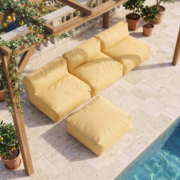 Modulares Garten-Lounge-Set aus drei Sitzelementen und einem Hocker mit hellgelbem Stoffbezug auf einer hellen Steinterrasse am Pool.