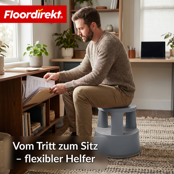 Ein Mann sitzt auf einem grauen Kunststoff-Rollhocker in einem hellen, organisierten Heimbüro und sortiert Dokumente. Floordirekt Logo.
