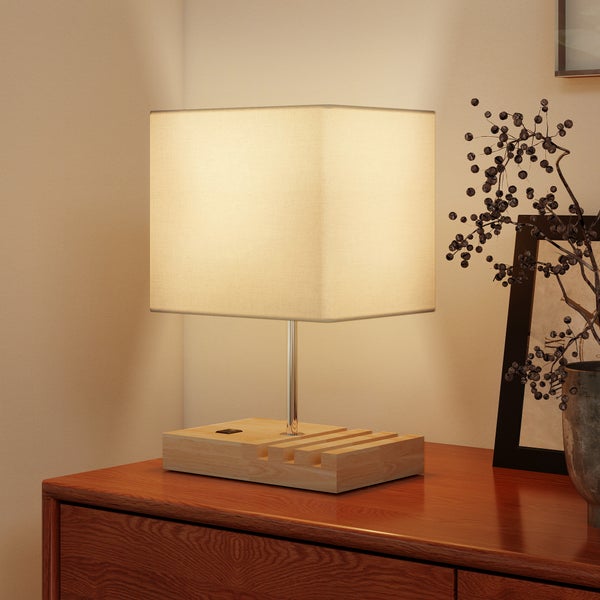 Tischleuchte mit eckigem Textilschirm, verchromtem Standrohr und Holzfuß mit integrierter Halterung auf einer Kommode.