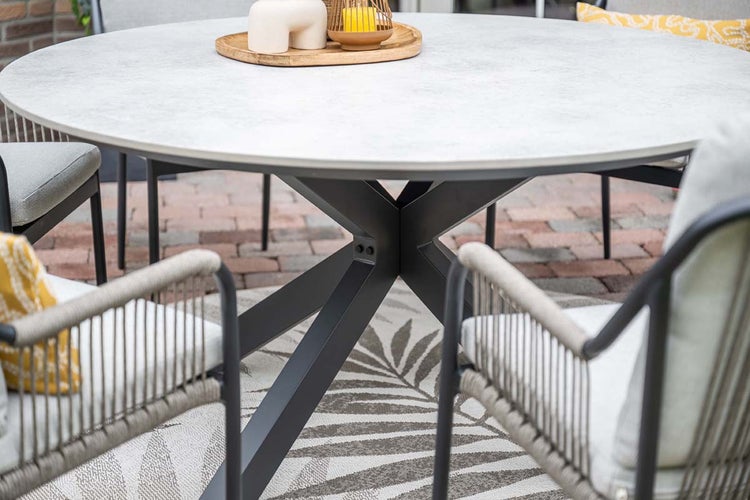 Runder Gartentisch mit Platte in Keramik-Optik und schwarzem Metall-Gestell, umgeben von Gartenstühlen mit Seilgeflecht auf einer Terrasse.