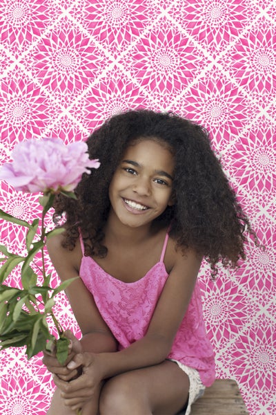 Lächelndes Mädchen mit Pfingstrose vor gemusterter Tapete