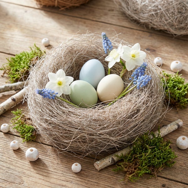 Osternest mit Ostereiern, Narzissen und Traubenhyazinthen dekoriert auf einem Holztisch mit Moos und Holzperlen als Frühlingsdekoration.