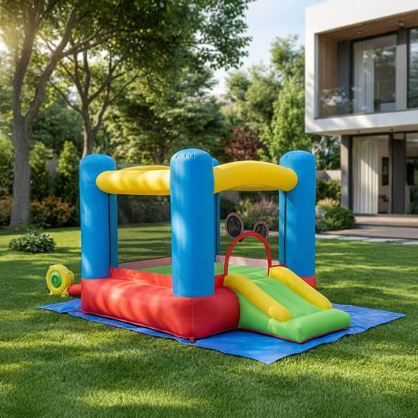 Farbenfrohe aufblasbare Hüpfburg mit Rutsche und Gebläse auf einem Rasen in einem Garten neben einem modernen Wohnhaus.