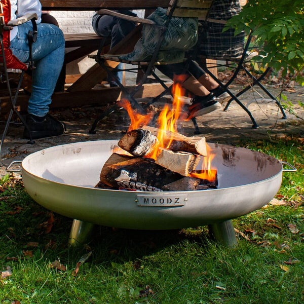 Feuerschale aus Edelstahl der Marke MOODZ auf einem Rasen im Garten mit brennendem Holzfeuer.
