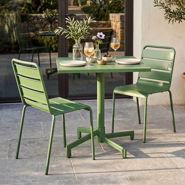 Grünes Gartenmöbel-Set aus Metall bestehend aus einem Bistrotisch und zwei Stühlen auf einer hellen Steinterrasse.