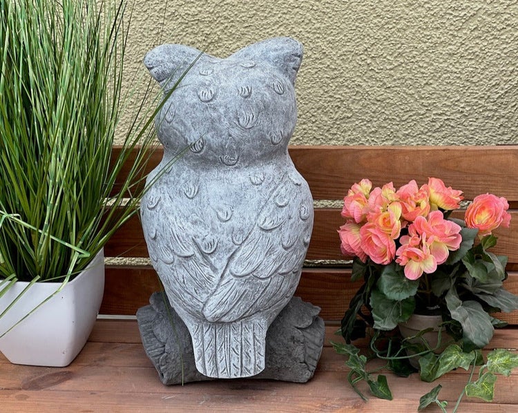 Gartenfigur Eule in Steinoptik von hinten auf einer Holzbank neben Topfpflanzen.