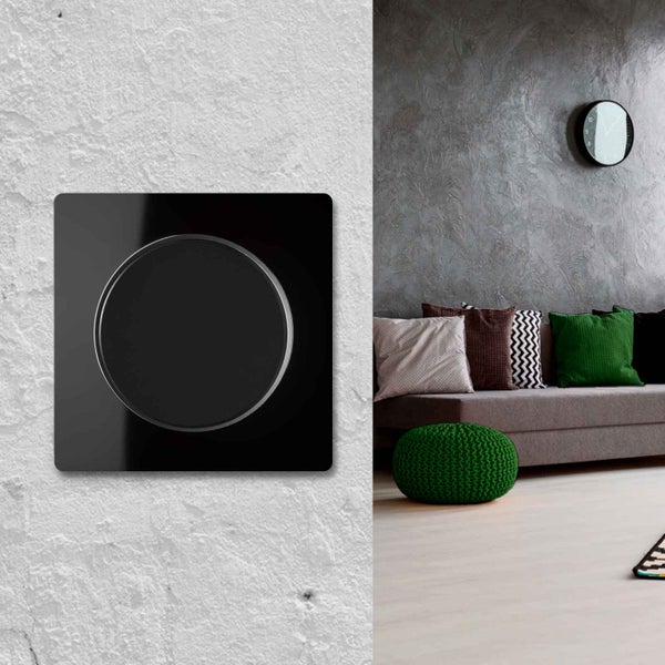 Moderner quadratischer Lichtschalter mit rundem Einsatz montiert an einer hellen Wand neben einem modernen Wohnzimmer