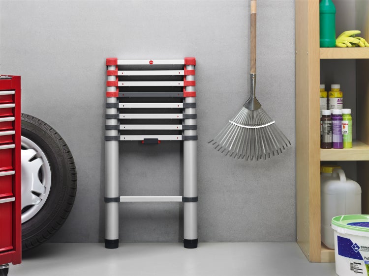 Aluminium-Teleskopleiter im Lagerraum neben Laubrechen, Werkzeugwagen und Regal