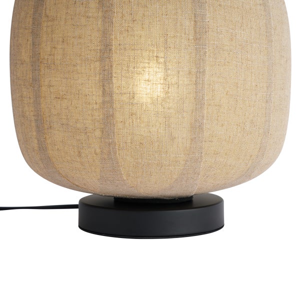 Tischleuchte mit rundem Schirm aus Textil in Leinenoptik und schwarzem Fuß, beleuchtet.