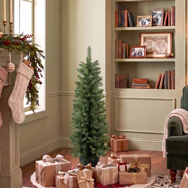 Künstlicher Weihnachtsbaum in einem festlich dekorierten Wohnzimmer mit Kamin Geschenken und Bücherregal.