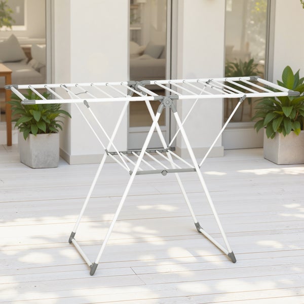 Weißer Flügelwäscheständer aus Metall auf einer hellen Holzterrasse mit grauen Kunststoffgelenken und unterer Ablageebene.