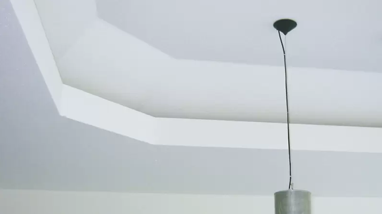 Weiße dekorative Deckenleiste aus Stuck in einem hellen Raum mit einer hängenden Pendelleuchte.