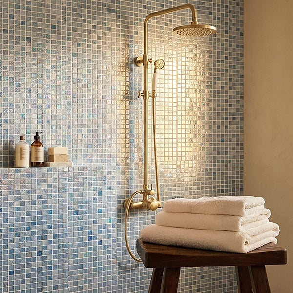 Moderne Duscharmatur in Messingoptik vor einer gefliesten Wand mit Mosaik und Holzhocker mit Handtüchern in einem Badezimmer.