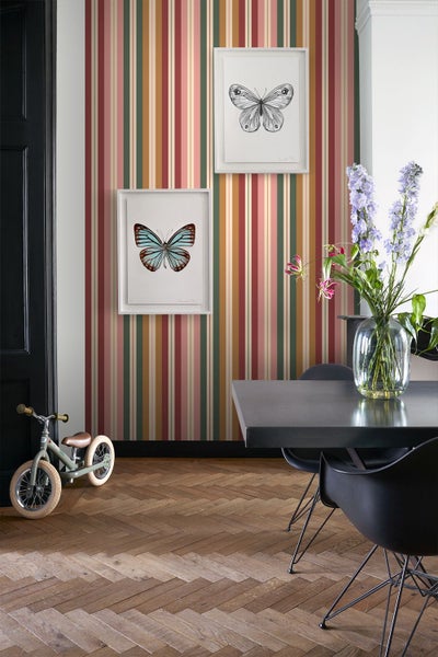 Gestreifte Tapete in einem Raum mit Fischgrätparkett, zwei Schmetterlingsbildern, einem Esstisch und einem Kinderlaufrad.