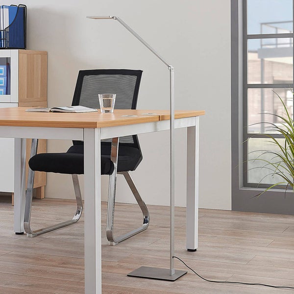 Moderne, silberne LED-Stehleuchte aus Metall über einem Schreibtisch in einem hellen, organisierten Arbeitszimmer mit schwarzem Bürostuhl.