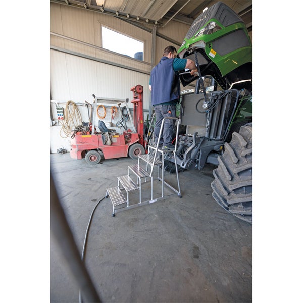 Ein Mechaniker nutzt eine Aluminium Arbeitsplattformtreppe zur Wartung eines Traktors in einer Werkstatt.