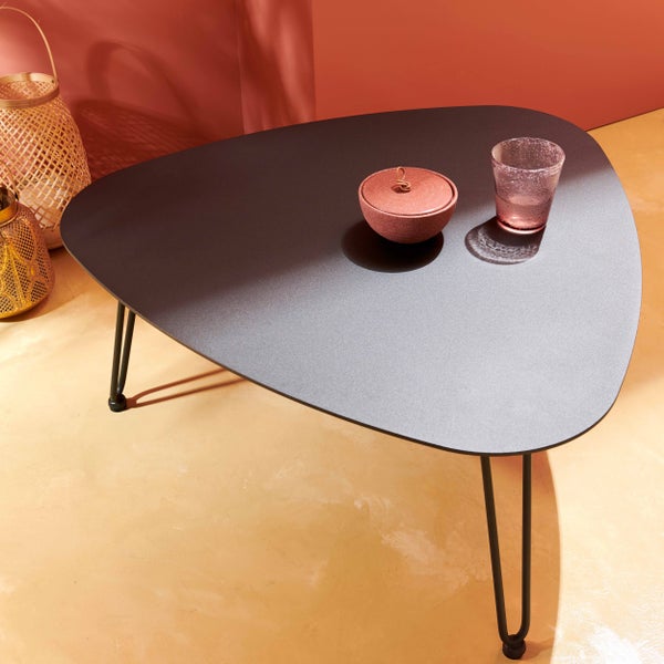 Dreieckiger schwarzer Couchtisch mit Metallbeinen, dekoriert mit Glas und Schale, neben dekorativen Laternen in modernem Ambiente.