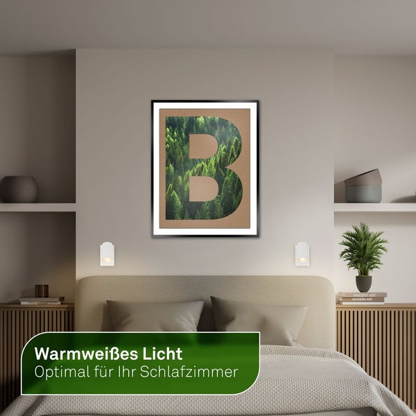 Schlafzimmer mit Bett, Nachttischen, Wandleuchten und einem gerahmten Buchstabenbild