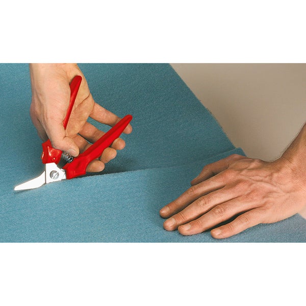 Eine Person schneidet mit einer roten Universalschere einen blauen Teppichboden.