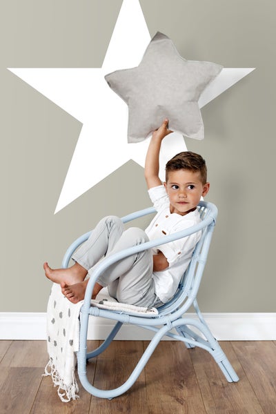 Junge sitzt in einem hellblauen Rattansessel mit einem Sternkissen in der Hand vor einem Wandbild mit Stern