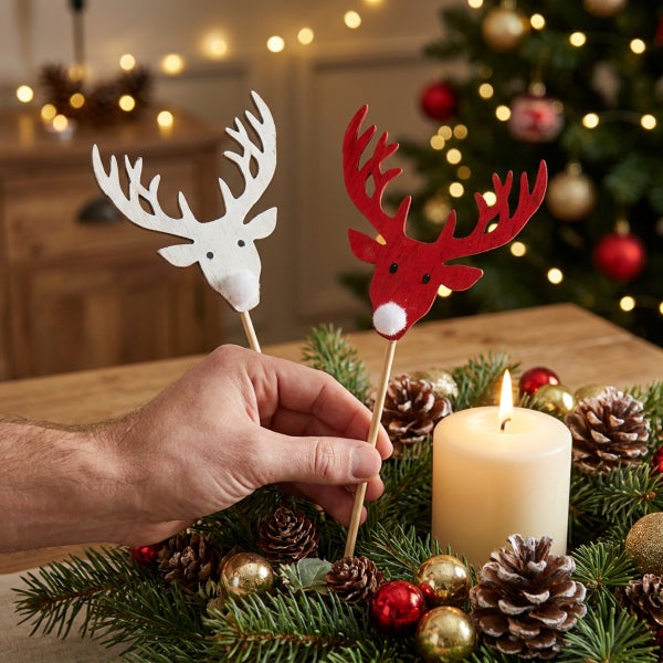 Hand platziert Holz Rentierstecker in einem Adventskranz mit Kerze und Tannenzapfen als weihnachtliche Dekoration.