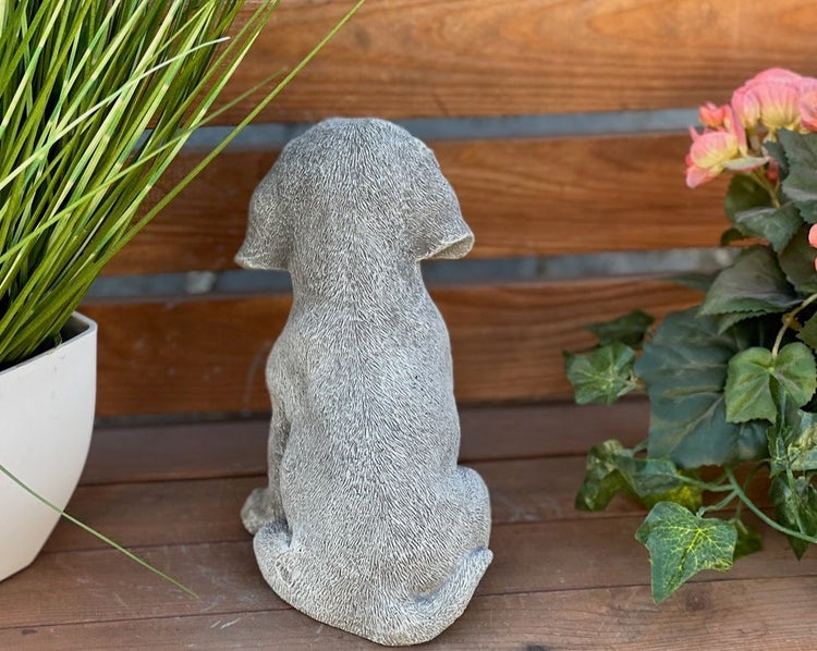 Gartenfigur sitzender Welpe von hinten in Steinoptik, dekoriert mit Pflanzen auf einer Holzoberfläche.