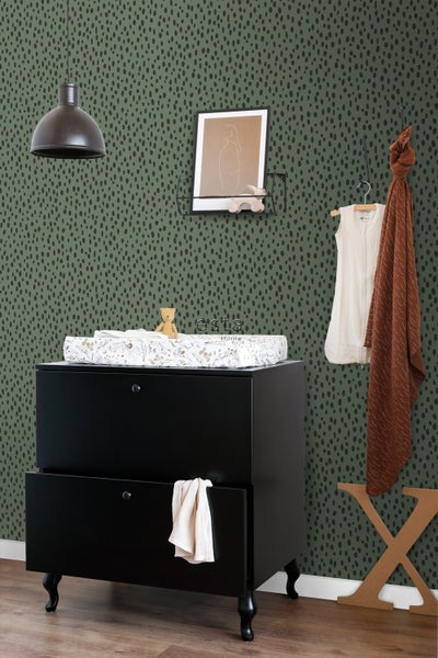 Ein Kinderzimmer mit einer Wickelkommode, einem Regal und einer Lampe vor einer gemusterten Tapete.