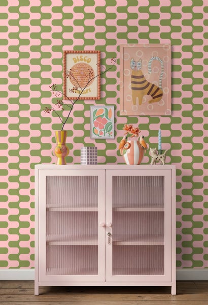 Vliestapete mit geometrischem Wellenmuster in Pink und Grün an einer Wand hinter einem pinkfarbenen Metallschrank mit Riffelglastüren.